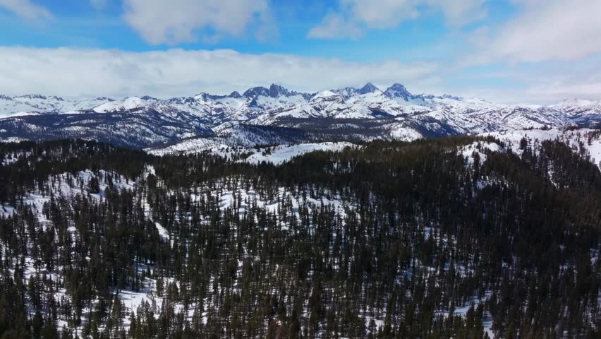 Banner peak Minaret Summit Pass Mammoth Mountains vista Parallax winter aerial drone California group jagged towering snow covered peaks sunny blue sky Inyo forest Sierra Nevada valley forward pan up