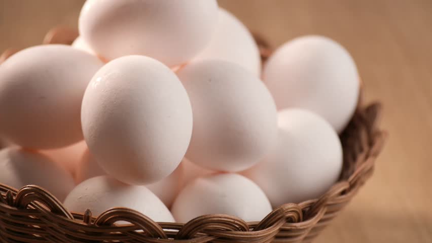 Fresh white eggs displayed in a woven basket on a wooden surface