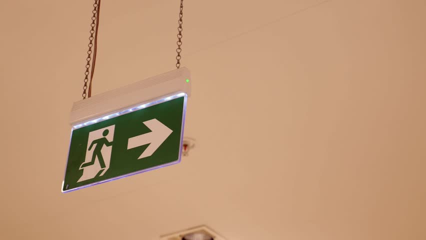 Emergency exit sign pointing right above the stairs indoors