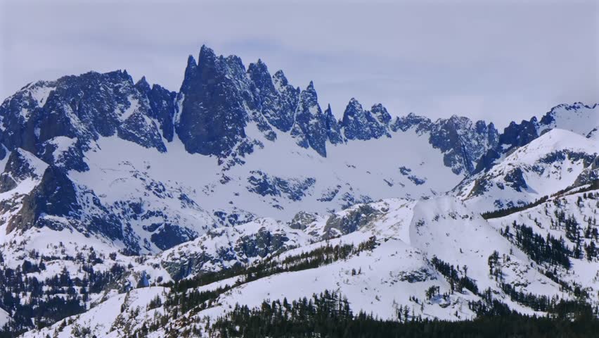 Banner peak Minaret Summit Pass Mammoth Mountains vista Parallax winter aerial drone California group jagged towering snow covered peaks sunny cloudy snow storm Sierra Nevada valley parallax right
