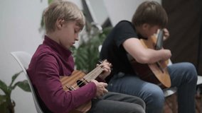 Two boys practicing guitar and ukulele together at home, playing music and having fun - Powered by Shutterstock - Get 15% off with code: PIKWIZARD15