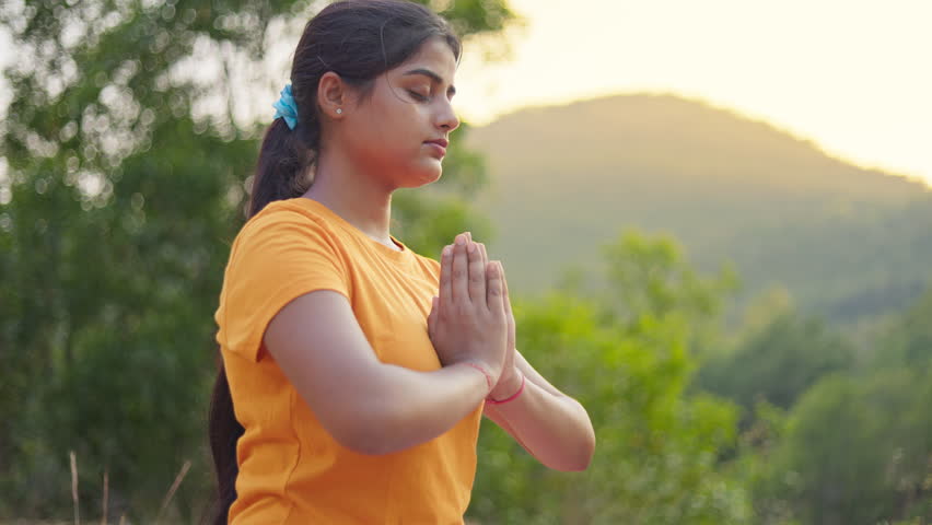 Pranamasana, meditation, yoga, young Indian woman making prayer pose hand gesture at outdoor in the early morning.