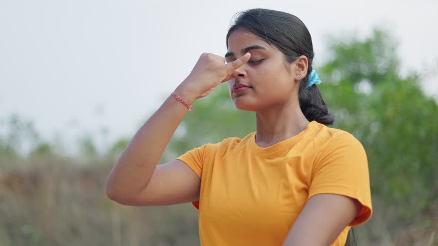 woman practicing alternate nostril breathing exercise with closed eyes at outdoor,