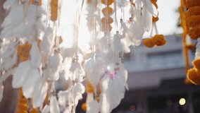 Close-up of marigold garlands and white feathers hanging in sunlight. Perfect for cultural events, festivals, wedding decor, spirituality, and traditional ceremonies. - Powered by Shutterstock - Get 15% off with code: PIKWIZARD15