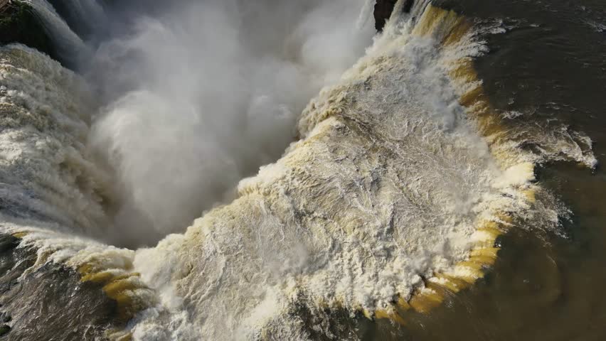 Iguazu Falls in Brazil drops over high cliffs. Water swirls at the bottom and rainforest stretches beyond. The force of the falls and the dramatic landscape with moving mist and sound