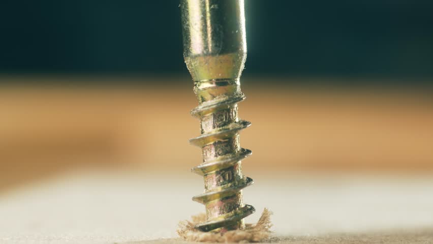 Close-up yellow self tapping screw tightening into wood by man using allen key. Macro view construction fastener rotating into surface with hex wrench by repairman. Brass hardware working into