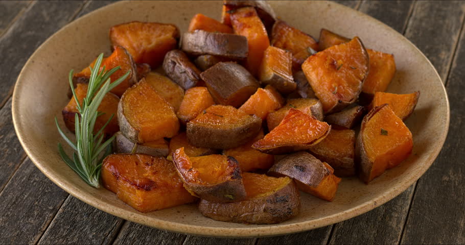 Platter of roasted sweet potatoes decorated with rosemary sprig. Table spin.