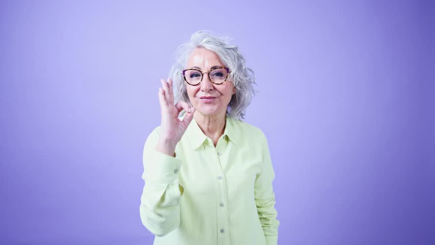 Senior woman showing ok sign on purple background