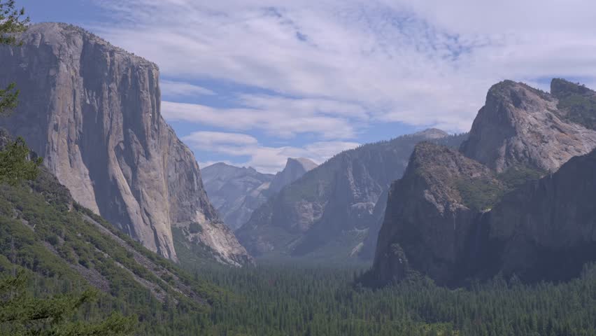 Footage of a medium shot from the famous Tunnel View overlook in Yosemite National Park, California, featuring the iconic granite cliffs of El Capitan and the distant peak of Half Dome.