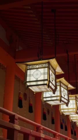 Illuminated Japanese lanterns hang in a row, showcasing intricate details and warm light within a traditional temple corridor. The scene evokes serenity and cultural richness.