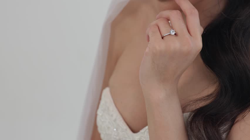 Asian Wedding ring and engagement ring hand of bride with long dark hair wearing white dress and veil showing love, commitment, diamond jewelry, and romantic moment of female celebration touching