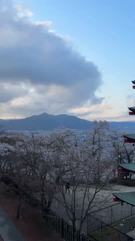 Stunning view of a three-story pagoda in Japan, adorned with cherry blossoms during spring. Mount Fuji is visible in the background. A serene and picturesque scene.