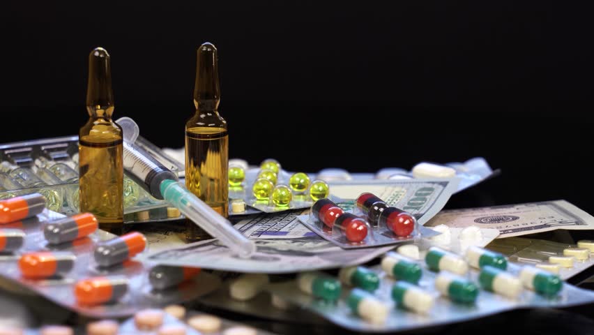 Ampoule Medications, Syringes, Pills and US Dollar Bills Rotate on Black Background. Medication costs. The rising costs of pharmaceuticals. Revenues of the pharmaceutical industry.  Part of a professional pharmaceutical production series. For matching clips and visual consistency, search for the unique series code: PHARMA-PROD-2026 or visit my dedicated collection: Pharmaceutical Manufacturing - PHARMA-PROD-2026