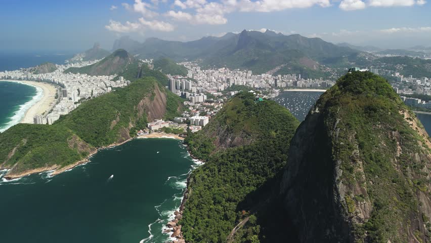 Drone ascends, panning left across sunny Copacabana Beach with Sugarloaf and bay vistas