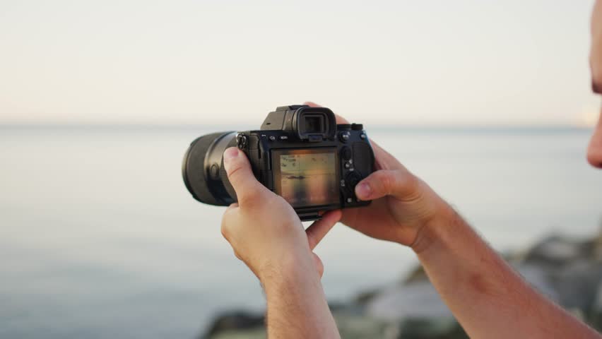 Young photographer capturing the sunset by the sea, holding a DSLR camera