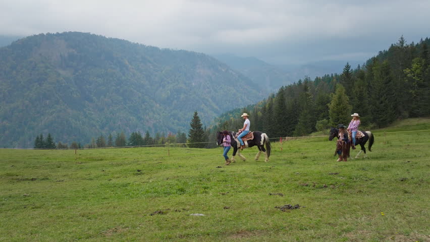 Couple taking a scenic horse ride through mountain landscapes at a ranch riding school, guided by cowgirls in traditional western wear, side view.