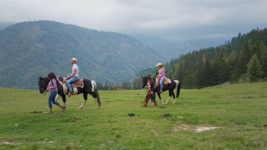 Couple taking a scenic horse ride through mountain landscapes at a ranch riding school, guided by cowgirls in traditional western wear, side view.