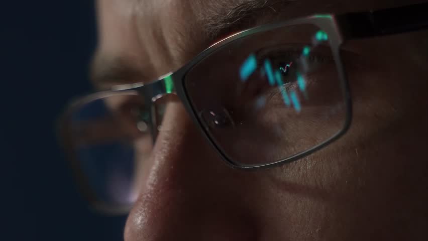 Close up of focused crypto trader wearing glasses closely analyzes cryptocurrency or stock market data with candlestick charts and financial graphs reflecting in his lenses, monitoring crypto trends.  - Powered by Shutterstock - Get 15% off with code: PIKWIZARD15