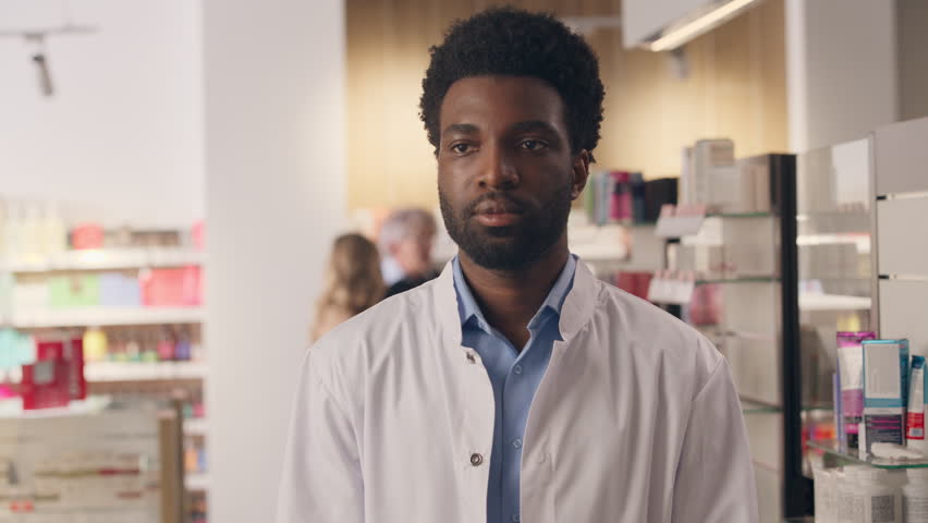 Portrait man African American guy pharmacist consultant smiling in drug store pharmacy health care products medication pharmaceutical help male seller medicine service doctor posing with crossed hands