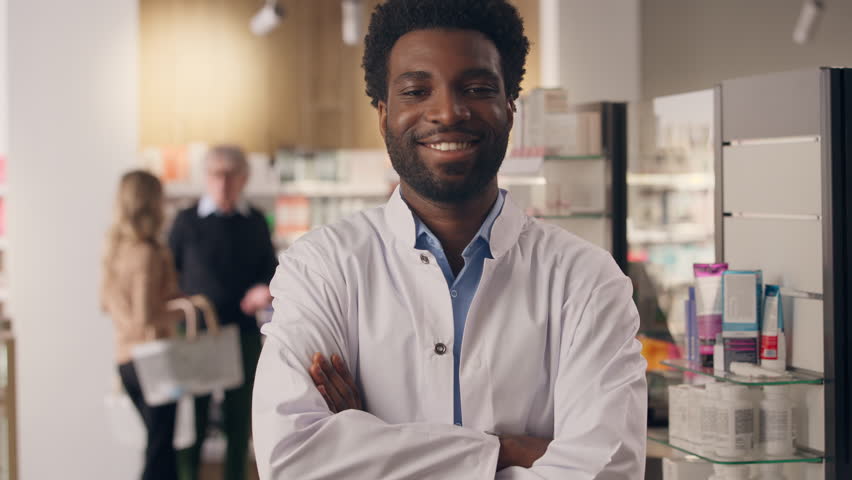 Portrait man African American guy pharmacist consultant smiling in drug store pharmacy health care products medication pharmaceutical help male seller medicine service doctor posing with crossed hands