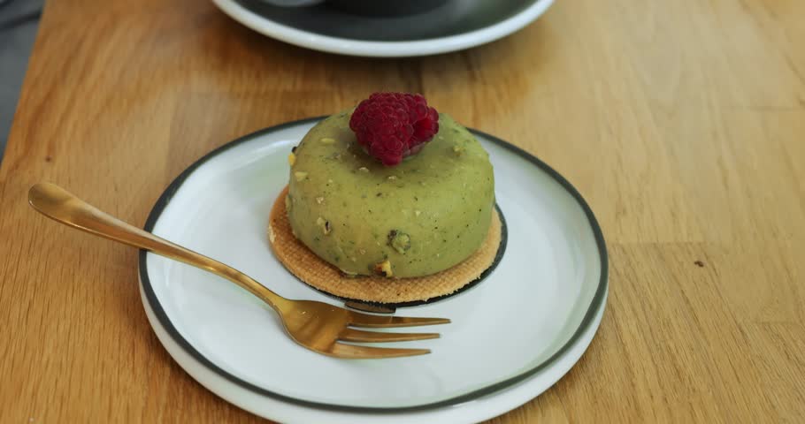 Tasty pistachio cake with fresh raspberry on top and cappuccino cup on wooden table. Healthy dessert and foamy coffee served in coffeeshop