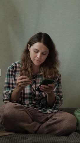 Vertical video. Mobile payment, online shopping. Woman paying online using bank card and mobile phone at home 