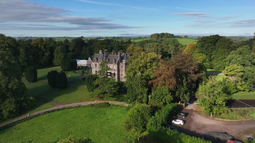 Castle Leslie, Glaslough, County Monaghan, Ireland, September 2022. Drone tracking left behind trees to reveal side sloping lawns of castle estate.