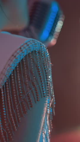Close-up of a singer in a white gown adorned with beaded fringe, performing with a vintage microphone. The soft, glowing lights in the background as she moves gently