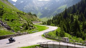 Drone tracks biker riding through Transfăgărășan road in Carpathian Mountains of Romania, surrounded by lush greenery and alpine landscape. - Powered by Shutterstock - Get 15% off with code: PIKWIZARD15