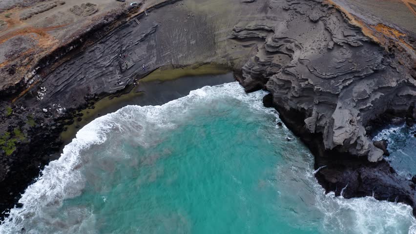 Aerial view of Green Sand Beach where vibrant turquoise waves roll onto unique olive-green sand, bordered by dramatic volcanic cliffs. This stunning Hawaiian coastline highlights rare formations.