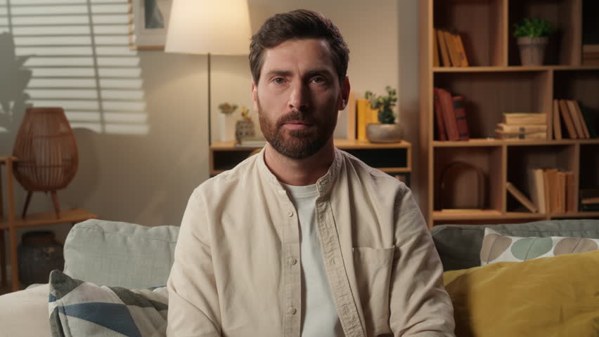 Sad frowning upset man Caucasian dissatisfied guy male home owner on couch showing thumb down gesture finger dislike hand gesture bad sign disapprove no negative result displeased looking at camera