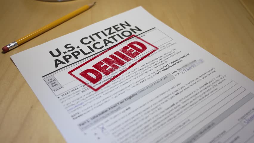 Close-up of a U.S. citizenship application form with a bold red “DENIED” stamp. A pencil rests nearby, highlighting the rejection of the naturalization request on a wooden desk surface. 14708  	