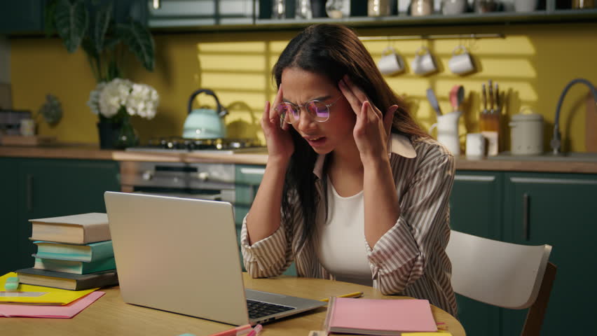Arabian businesswoman work online laptop at home kitchen girl tired exhausted student freelancer suffer headache stress overwhelmed Indian woman massaging head pain studying computer overwork migraine