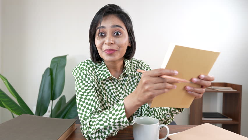 A cheerful woman with short hair holds a notebook and pencil and looks amazed with a friendly smile