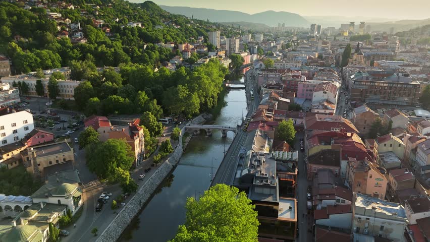 Scenic beauty of Sarajevo with aerial views of the Miljacka River and vibrant city life during sunset. Flying over summer Sarajevo, Bosnia and Herzegovina