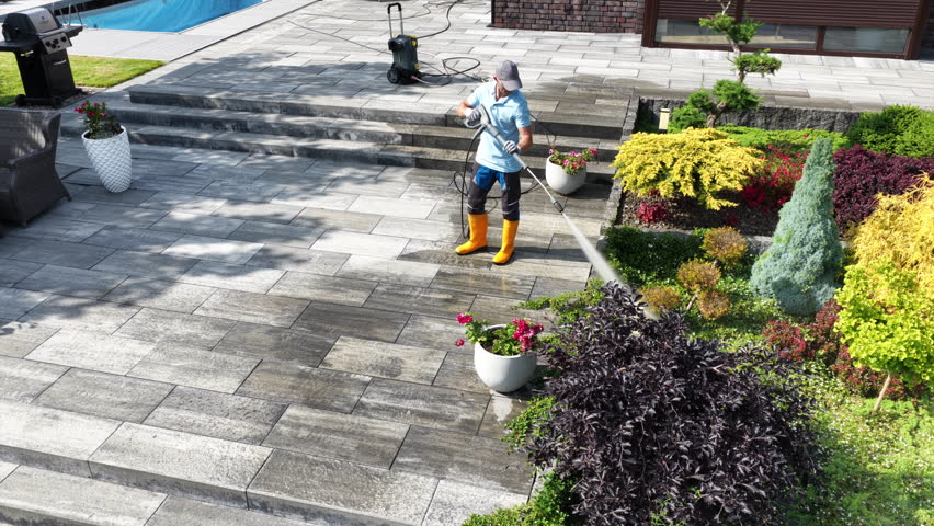A person waters vibrant plants in a well-maintained yard, surrounded by colorful foliage and a swimming pool on a bright day.