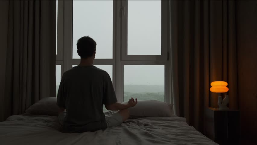 Man meditating in silence by the window on a rainy day