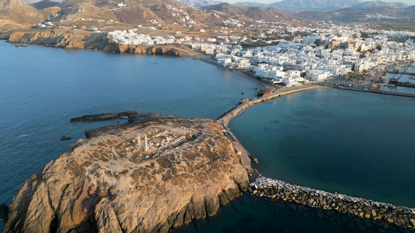 Aerial view of the Temple of Apollo standing on a rocky outcrop connected by a causeway to the town, contrasting with the deep blue sea, Naxos, Naxos, Greece.