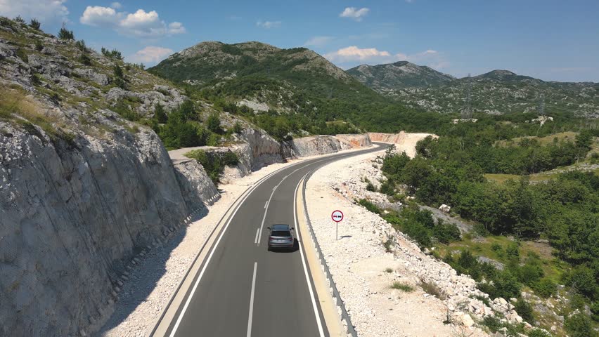 Aerial view of a car driving on a new highway with picturesque green mountains in the background