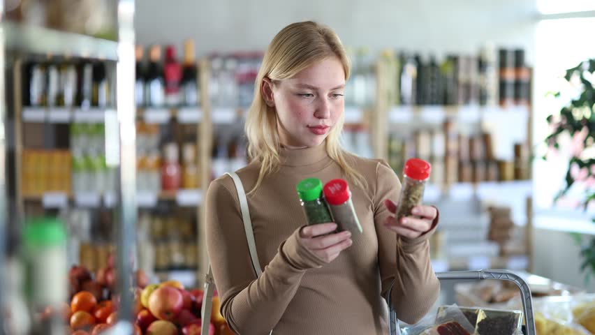  Young woman buyer chooses spices and seasonings in jar in grocery store