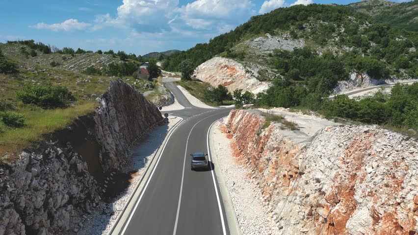 The car is driving along a mountain road, with mountain slopes on the sides. Aerial view.
