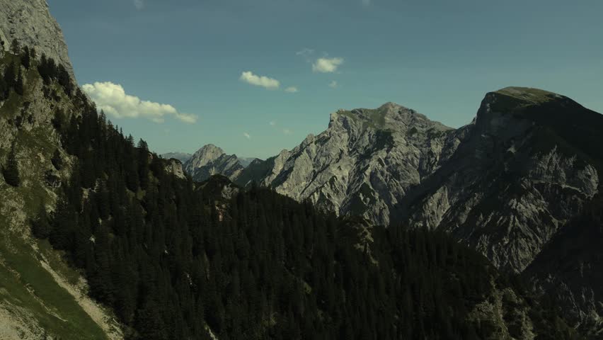 Aerial view of the majestic mountain range under a clear sky, showcasing the rugged terrain and lush forests of Tirol, Austria.