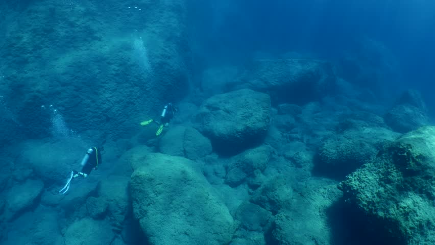 underwater scenery of big rocks topography scuba divers exploring
