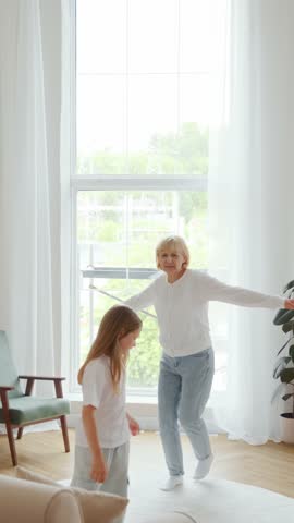 Wide vertical shot: in a bright living room, a smiling girl runs across the floor and jumps into her grandmas arms. Emotional reunion moment. Shot in vertical format, ideal for mobile stories. 4k