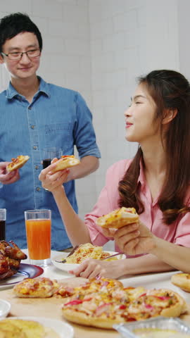 Vertical Screen : Happy young friends group having lunch at home. Asia family party eat pizza food and laugh enjoy meal sitting at dining table together at house. Celebration holiday and togetherness.