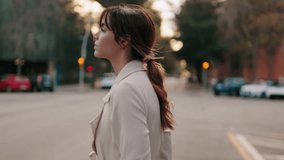 A young woman walks down a city street at sunset. She is wearing a stylish trench coat and has her hair tied back in a ponytail. - Powered by Shutterstock - Get 15% off with code: PIKWIZARD15