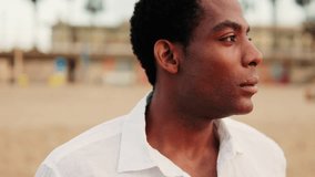Young African American man with short hair stands on a beach in a white linen shirt, staring into the distance. - Powered by Shutterstock - Get 15% off with code: PIKWIZARD15