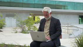 Zoom in shot of confident senior businessman smiling while using laptop outdoors near modern building, expressing positive attitude in professional environment - Powered by Shutterstock - Get 15% off with code: PIKWIZARD15
