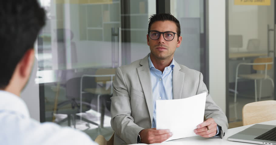 Young Latino HR manager in suit hold cv listens male applicant speaking about education, competence, qualification and professional skills during job interview. Negotiations, formal meeting in office
