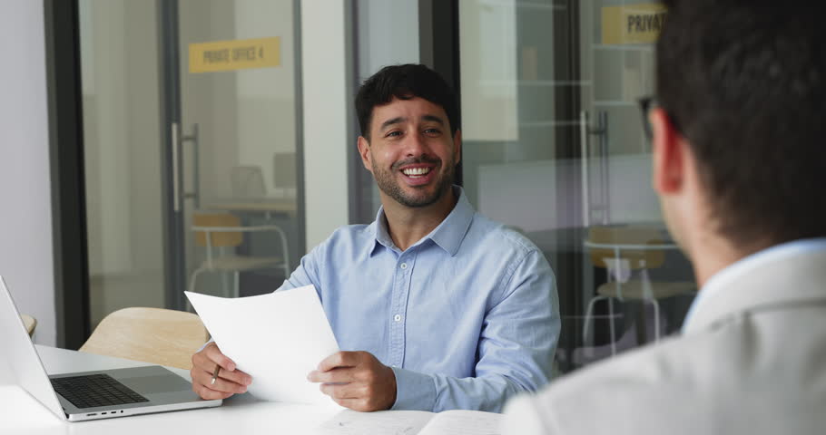 HR manager interviewing male applicant seated at desk, holds resume, asks about education, professional skills and experience during formal meeting job interview. Human resources, company staffing
